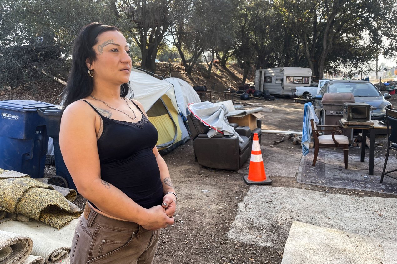 A photo shows Daisy Gonzalez posing for a portrait outside near the encampment where she lives.