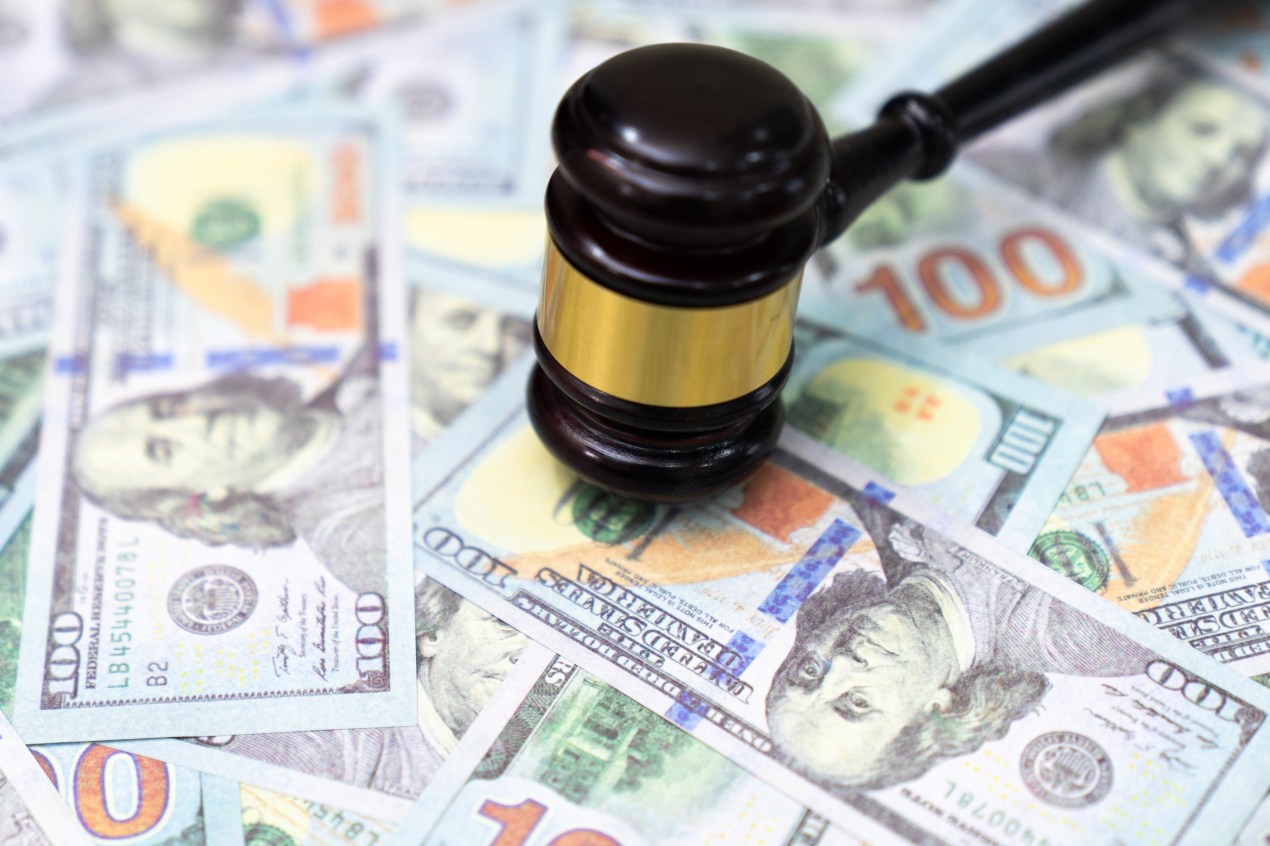 U.S. 100 bills strewn across a table with a gavel positioned downward to signify a court case