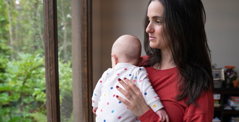 A photo shows a woman holding her infant child while facing a window.