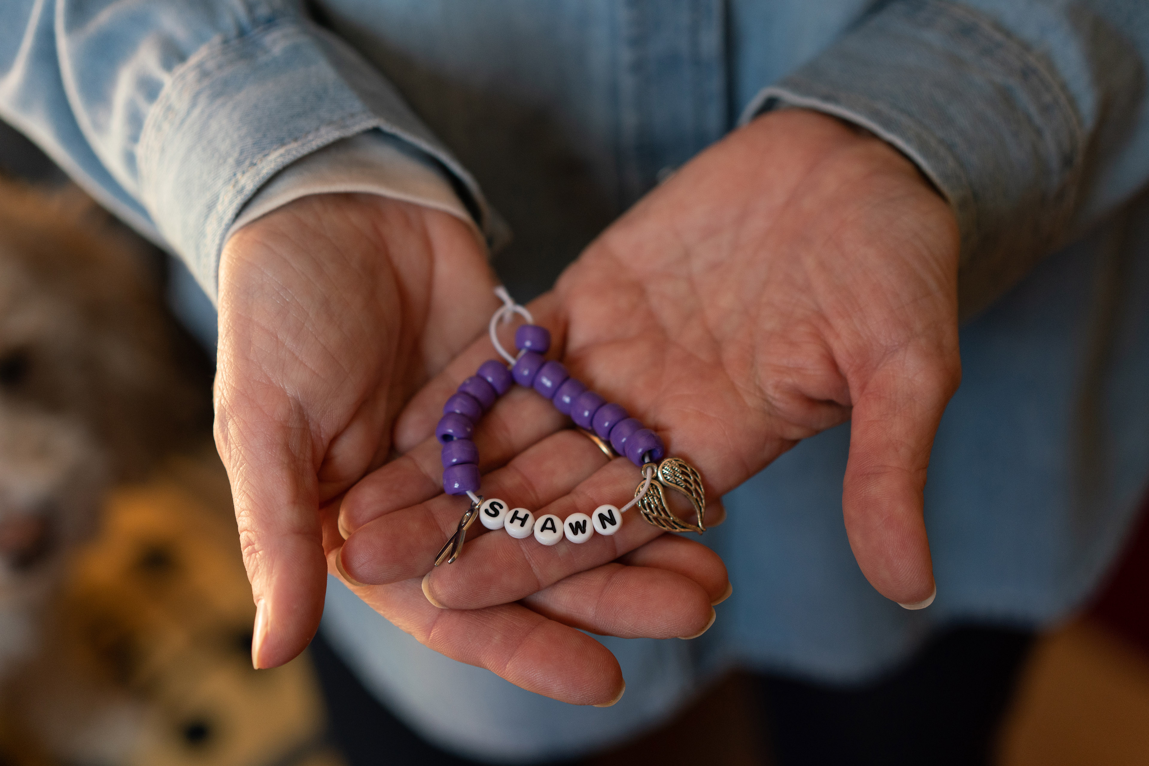 Marianne Sinisi, of Altoona, Pennsylvania, holds in her two palms a purple beaded bracelet with the observe 